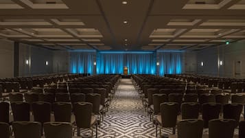 A conference room with rows of chairs, a patterned carpet, and a stage with blue curtains.
