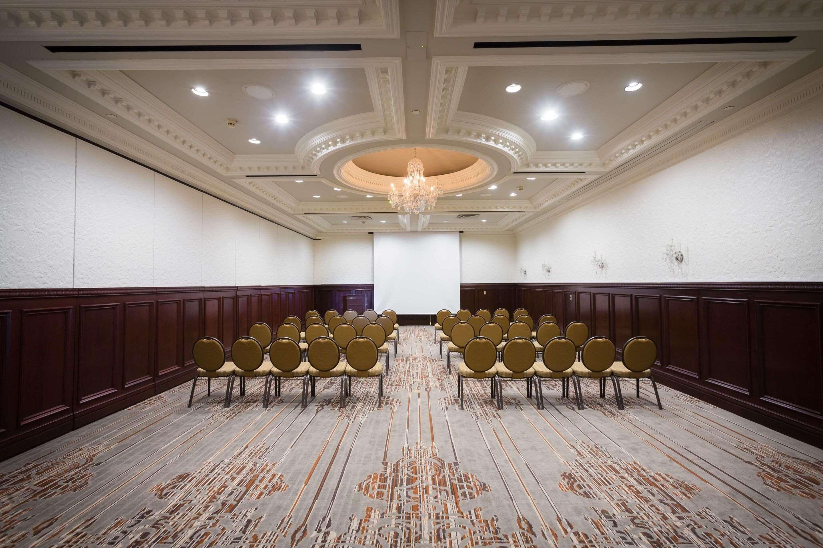 A conference room with rows of chairs, a large screen, and a chandelier.