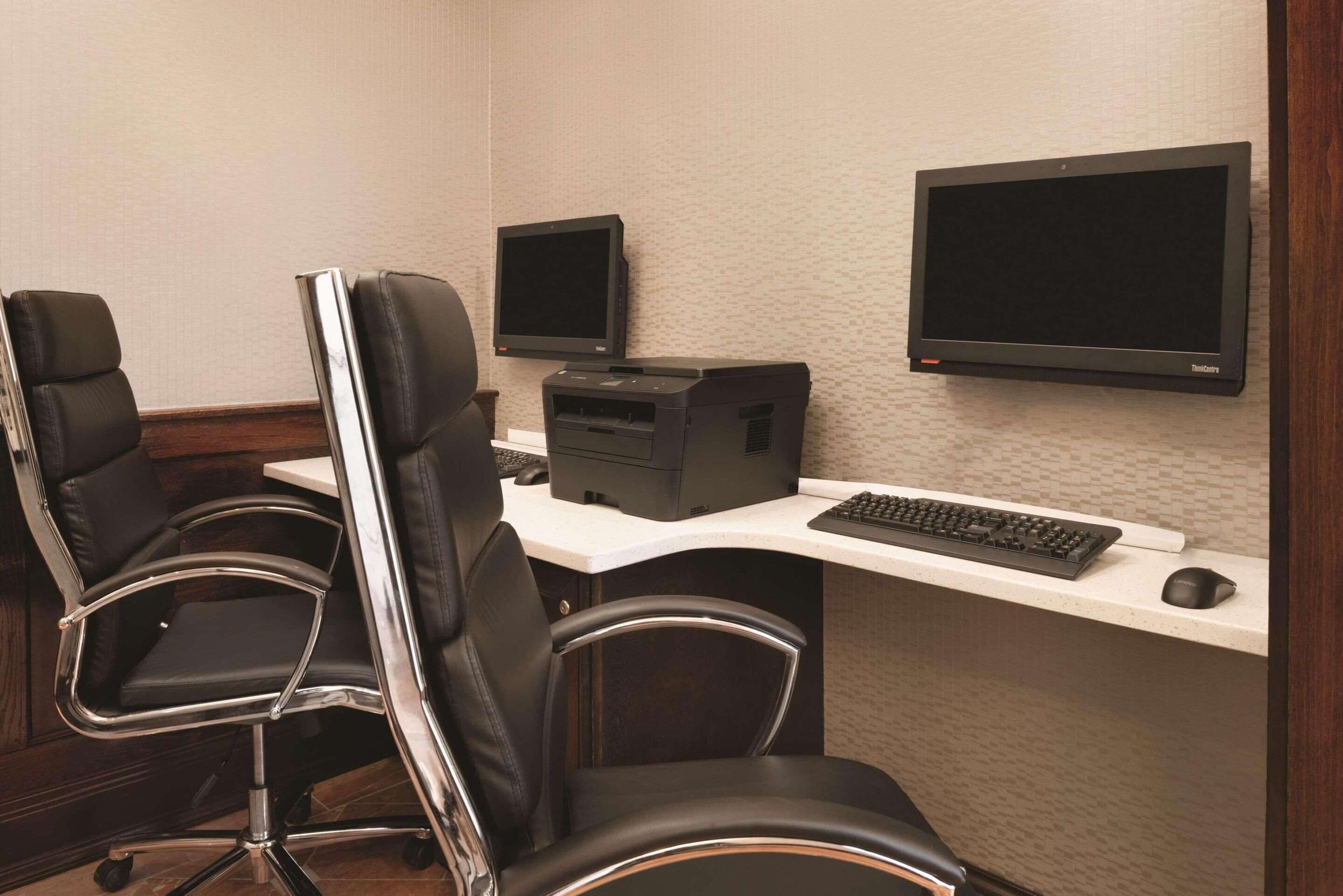 Una sala de conferencias con dos sillas de cuero negro, un escritorio blanco, un ordenador de sobremesa, dos monitores y un teclado.