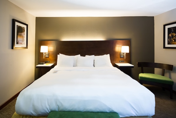 A hotel room with a large bed, two bedside tables with lamps, a green chair, and framed artwork on the walls.