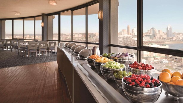 A buffet with various fruits and a city view through large windows. - Radisson Hotel Cincinnati Riverfront (Covington)
