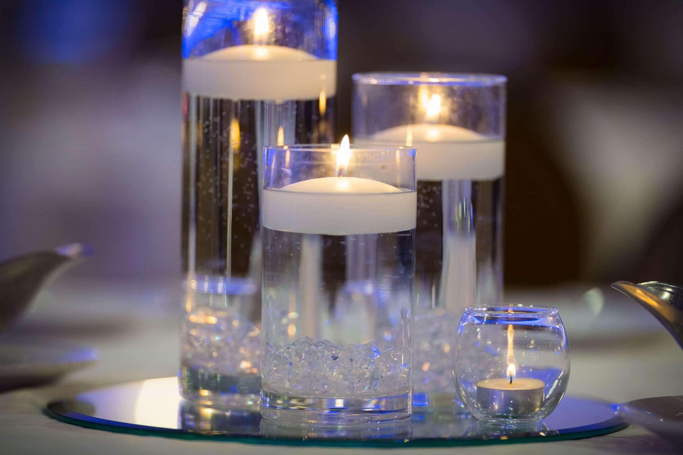 Three glass candle holders with candles, one with ice cubes and one with a smaller candle.