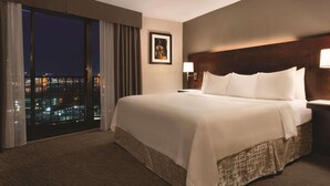 A hotel room with a large bed, a nightstand, a framed picture on the wall, and a view of the city at night through the window. - Radisson Hotel Cincinnati Riverfront (Covington)