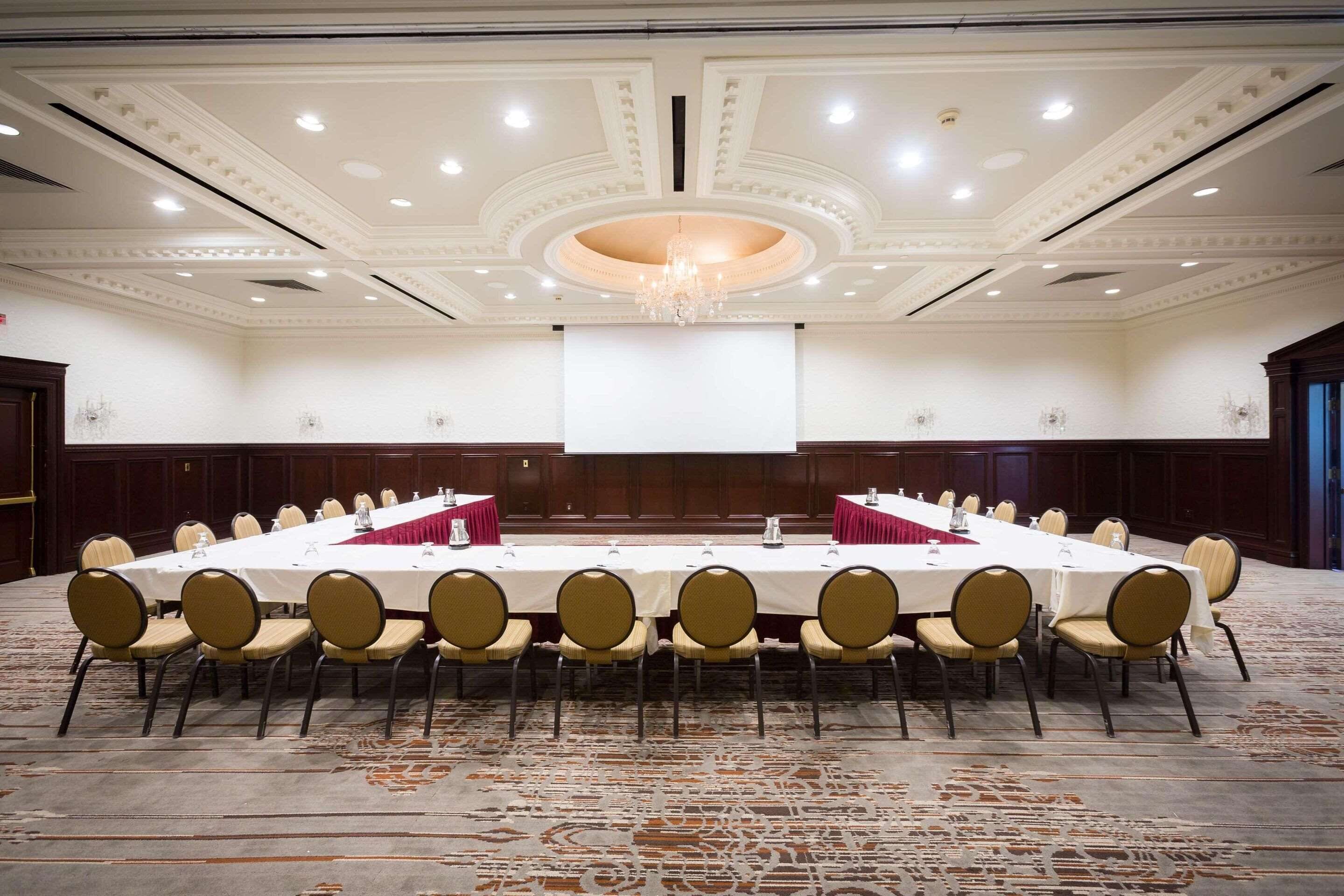 A conference room with a long table, chairs, a projector screen, and a chandelier.