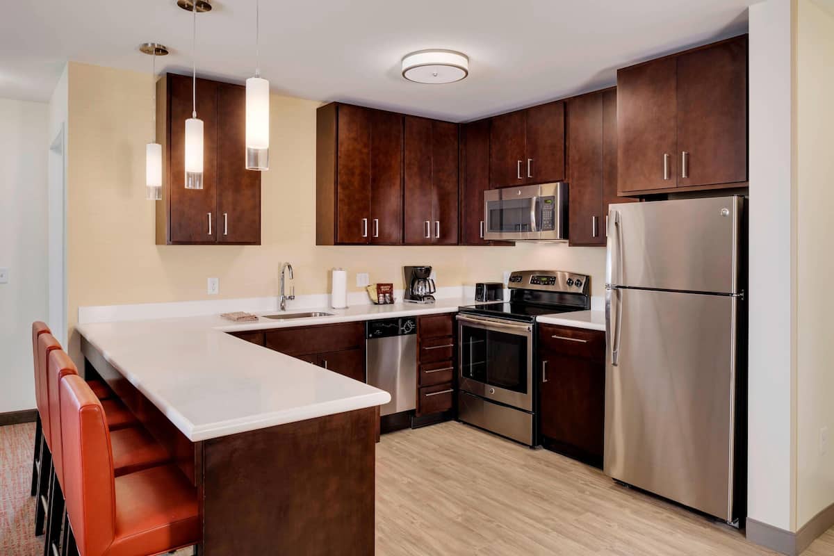 A modern kitchen with dark wooden cabinets, stainless steel appliances, and a white countertop.
