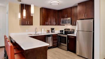 Una cocina moderna con armarios de madera oscura, electrodomésticos de acero inoxidable y encimera blanca.