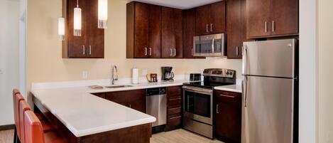 A modern kitchen with dark wooden cabinets, stainless steel appliances, and a white countertop.