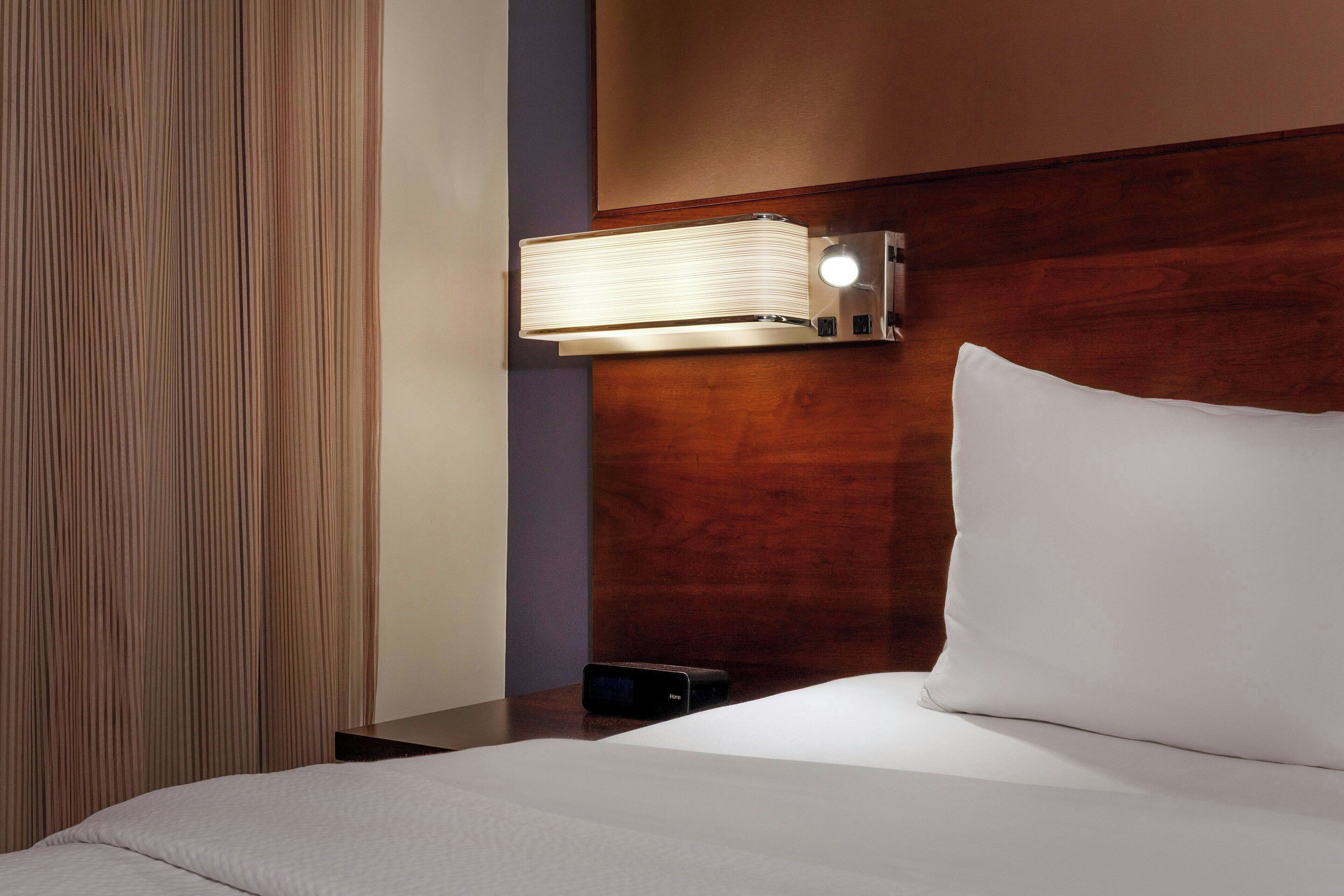 Una camera d'albergo con un letto, un comodino, una lampada e una testiera in legno.