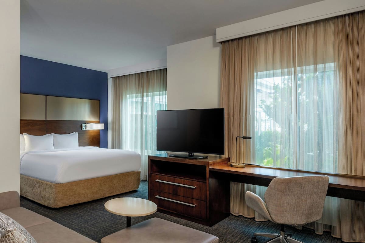 A hotel room with a bed, a desk with a TV, a chair, and a small table.