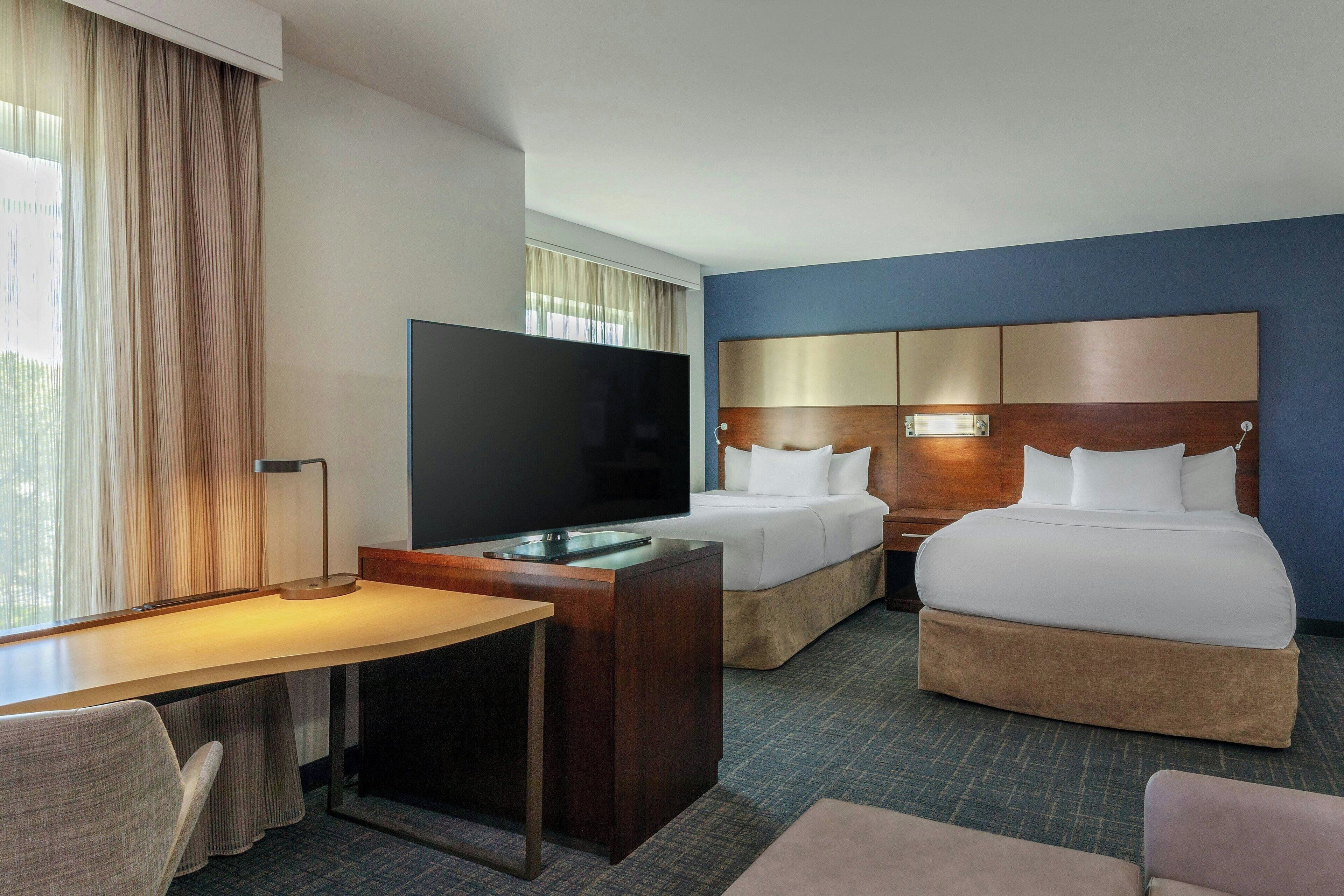 Une chambre d’hôtel avec un lit, un bureau, une télévision et une fenêtre avec des rideaux.