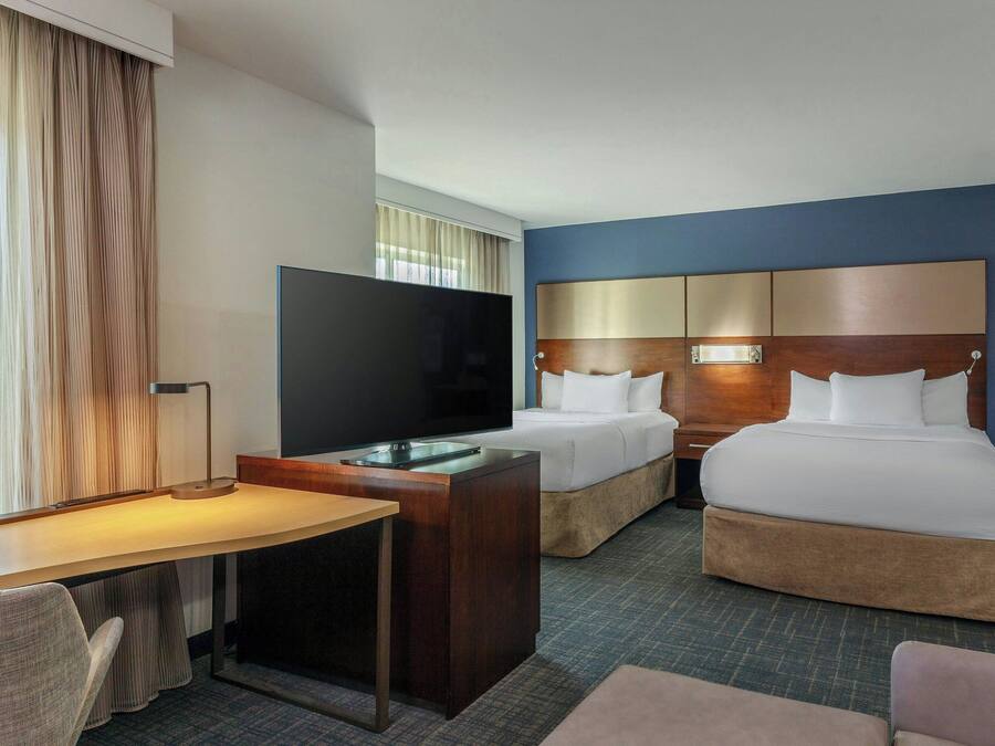 Une chambre d’hôtel avec un lit, un bureau, une télévision et une fenêtre avec des rideaux.