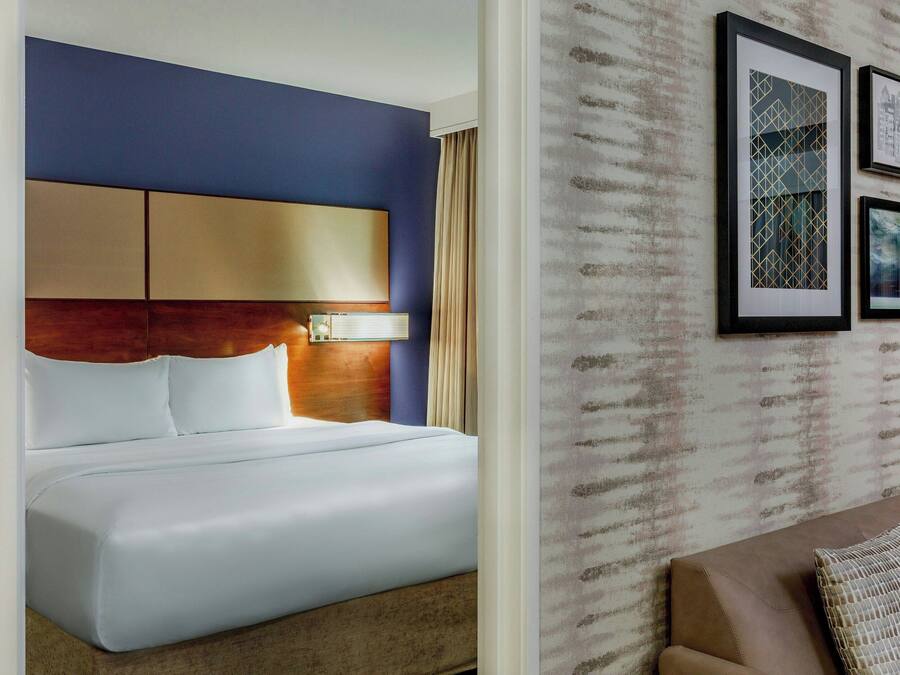 A hotel room with a large bed, a headboard with a light fixture, and a wall with framed artwork.
