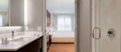 A hotel room with a bathroom, a bed, and a shower.