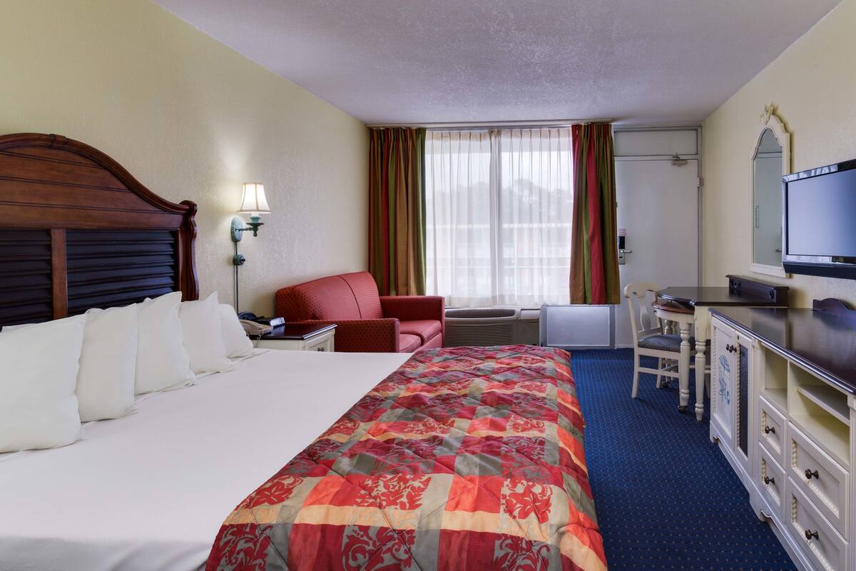 Une chambre d’hôtel avec un grand lit, un bureau avec une chaise, une télévision et une fenêtre avec des rideaux.