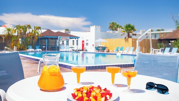 A poolside table with a pitcher of orange juice, three drinks, a plate of fruit, and sunglasses. - Seralago Hotel and Suites Main Gate East (Kissimmee)