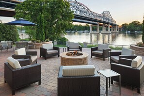An outdoor patio with wicker furniture, a fire pit, and a view of a river and bridge. - Courtyard by Marriott La Crosse (La Crosse)
