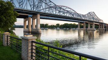 A steel bridge over a calm river with a grassy bank and a metal railing.