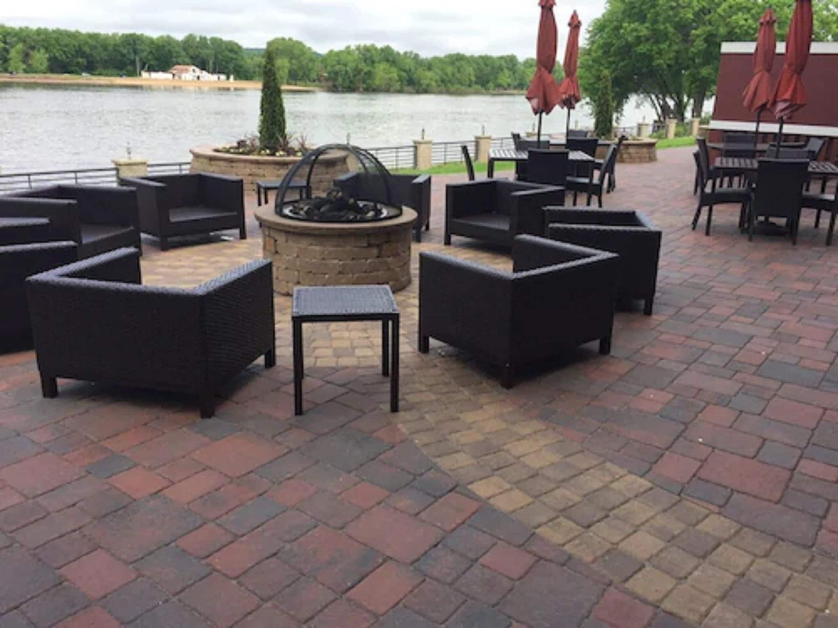 An outdoor patio with wicker furniture, a stone fire pit, and a view of a lake.