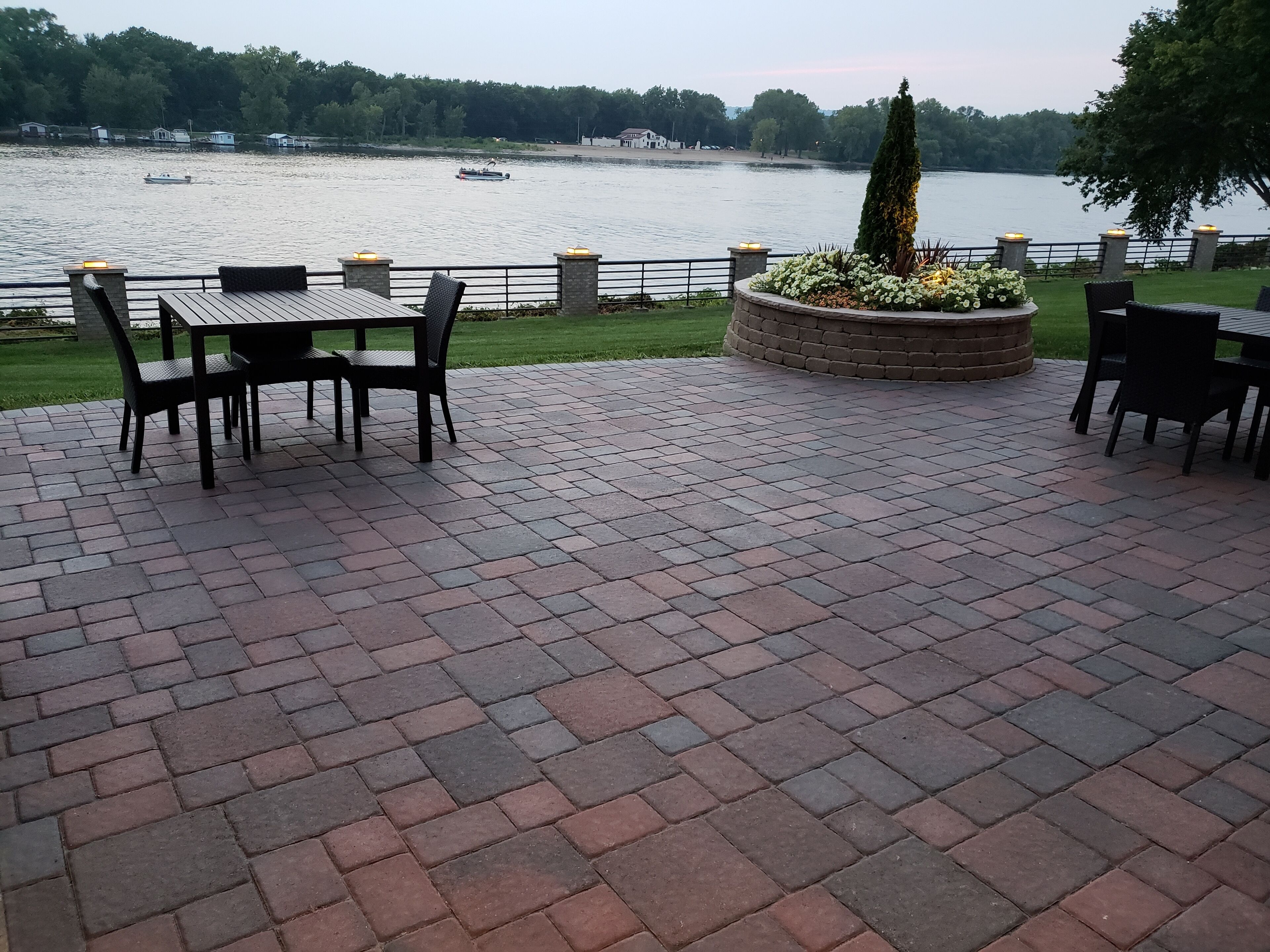 A patio area with brick flooring, outdoor furniture, and a view of a lake with boats.