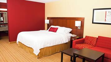 A hotel room with a bed, a red sofa, a small table, and a wall-mounted lamp.