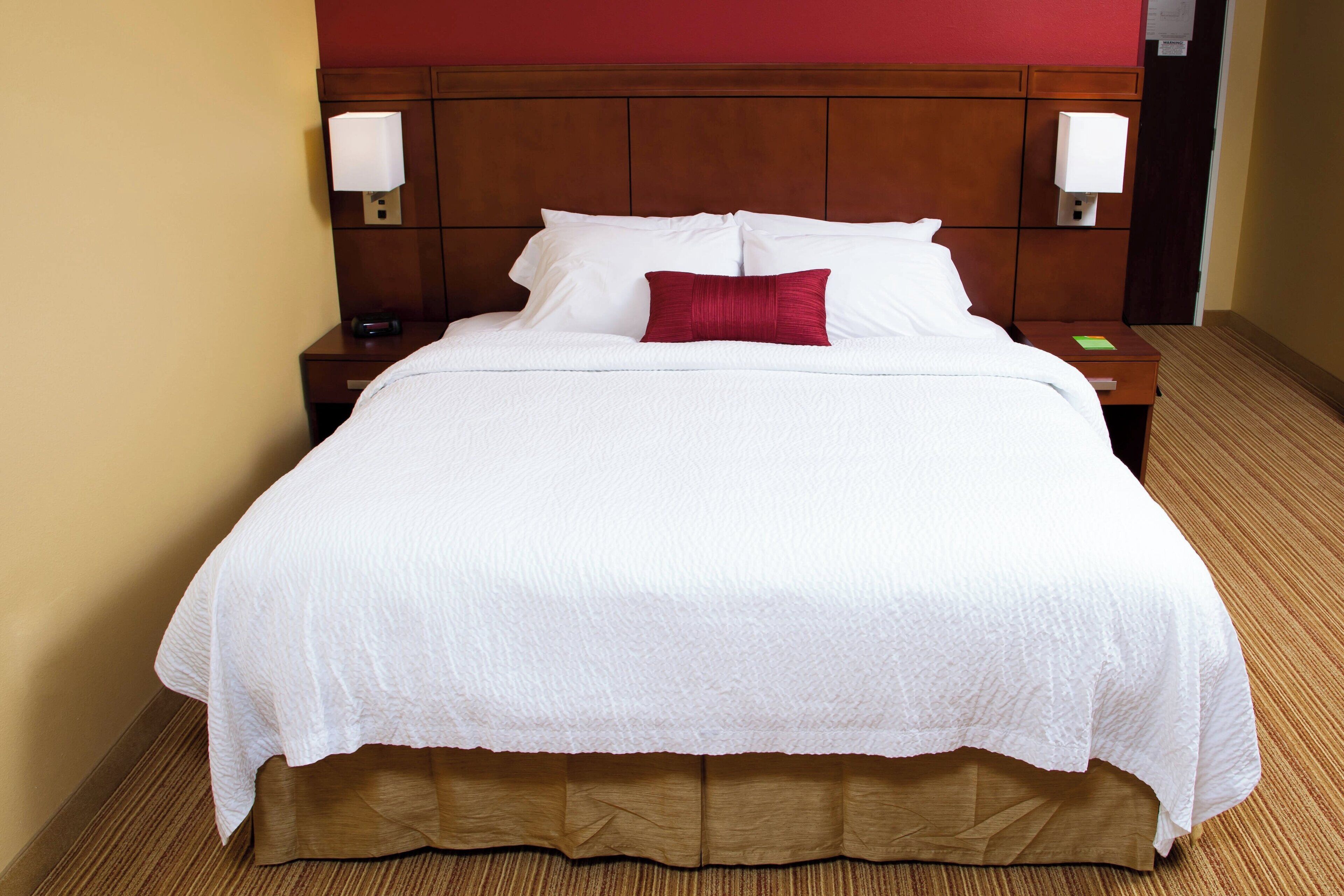 A neatly made bed with white linens, a wooden headboard, and two bedside lamps.