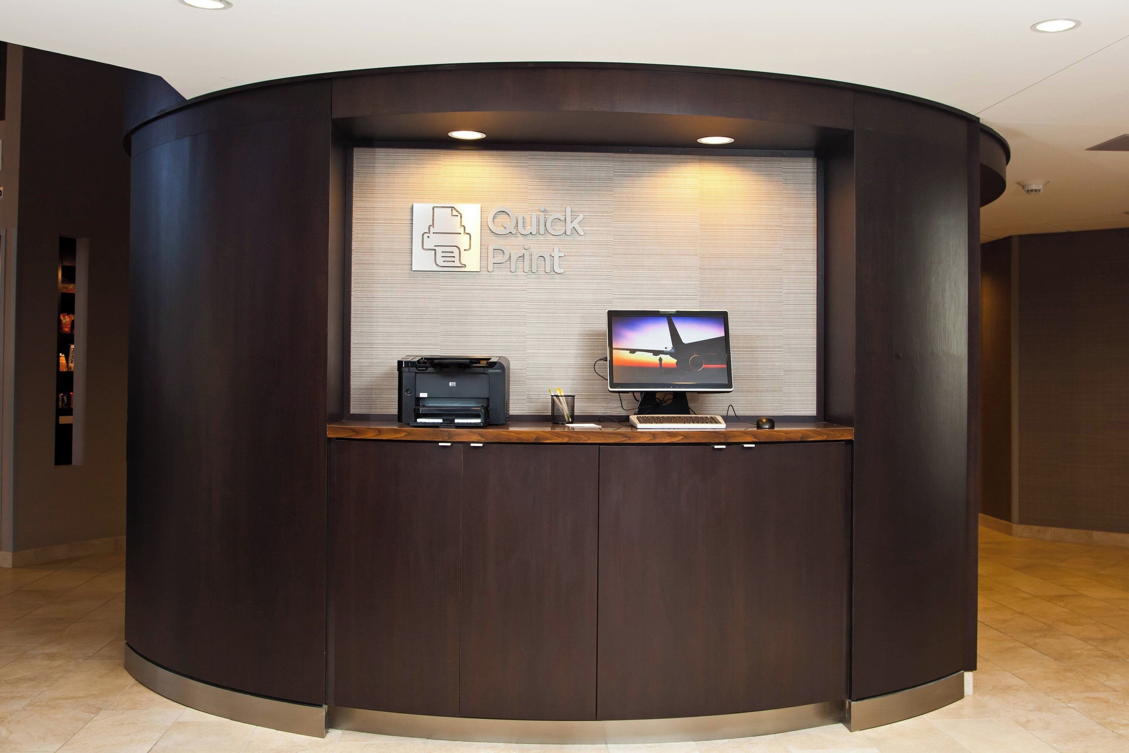 Un mostrador de recepción con un monitor que muestra una imagen de atardecer, una impresora y un letrero que dice "Quick Print".