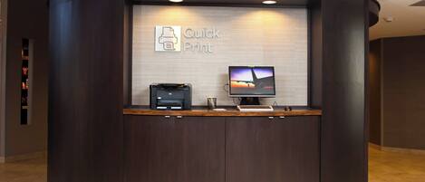 Un mostrador de recepción con un monitor que muestra una imagen de atardecer, una impresora y un letrero que dice "Quick Print".