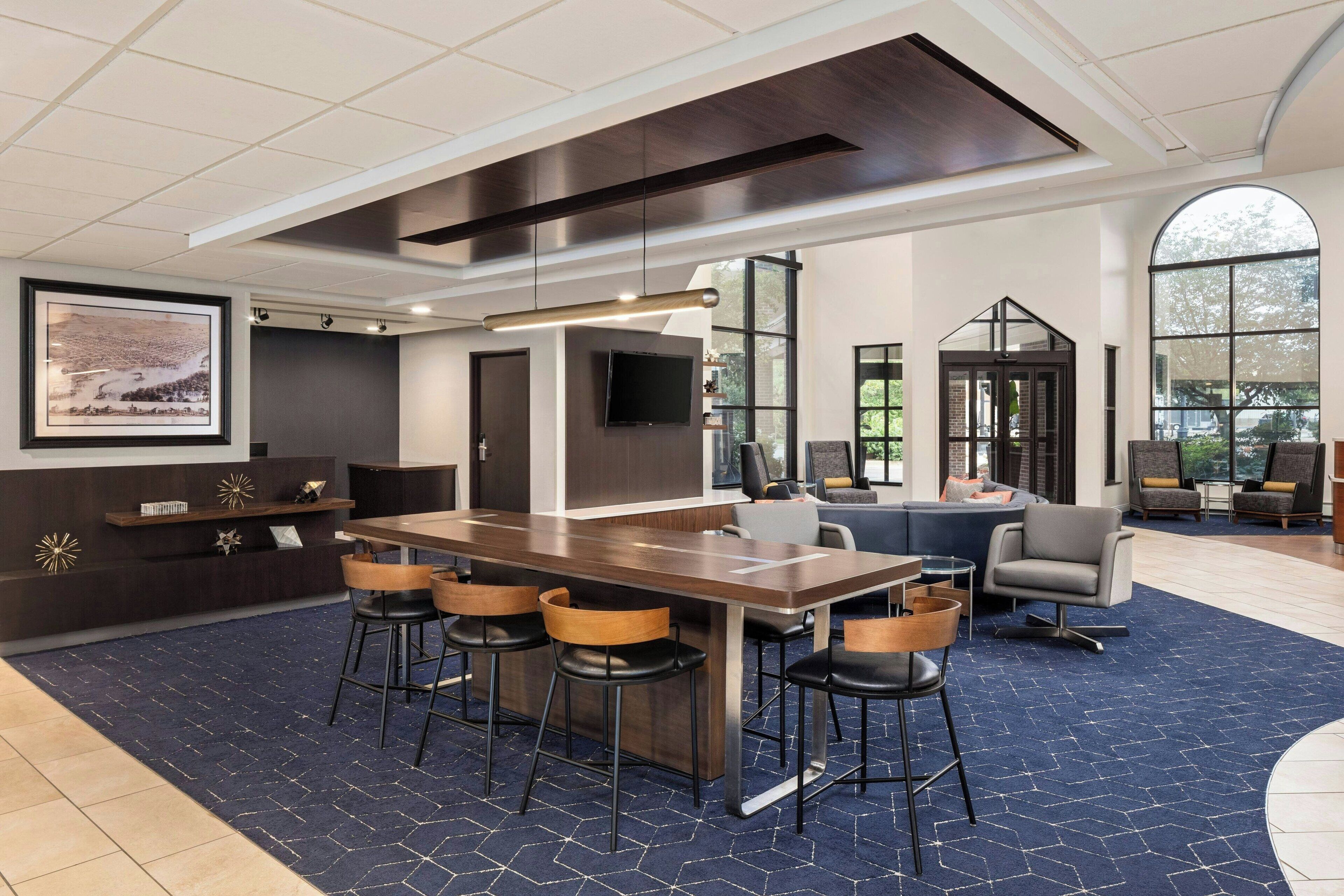A modern hotel lobby with a large bar area, comfortable seating, and large windows offering views of the outdoors.