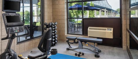 A gym with exercise equipment, a blue mat, and large windows with a view of a bridge.