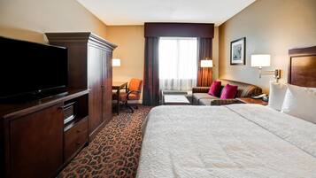 Una habitación de hotel con una cama grande, televisor, escritorio y una silla.