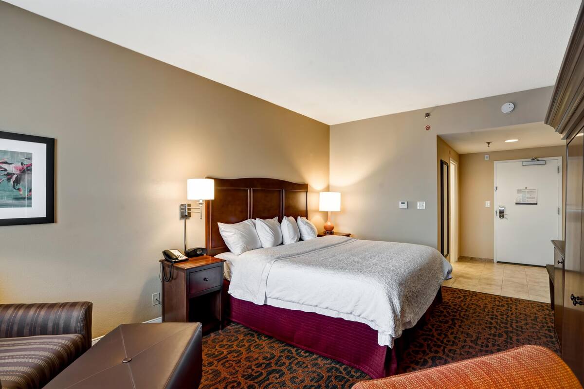 Habitación de hotel con una cama grande, dos lámparas de noche, una mesita de noche, una silla y una alfombra estampada.