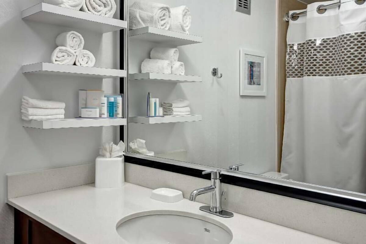 Un baño con lavamanos, espejo, toalleros y cortina de ducha.