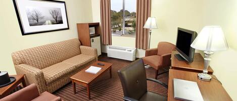 A hotel room with a sofa, two armchairs, a desk with a laptop, a telephone, and a television.