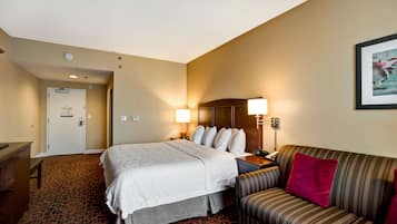 A hotel room with a bed, a sofa, a desk, a lamp, and a door.