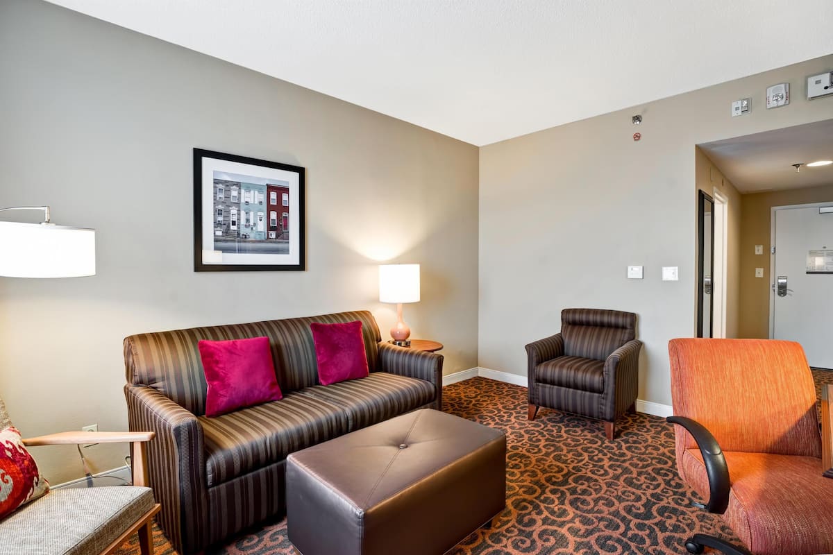 Una habitación de hotel con un sofá a rayas, dos sillones, una mesita y una alfombra estampada.