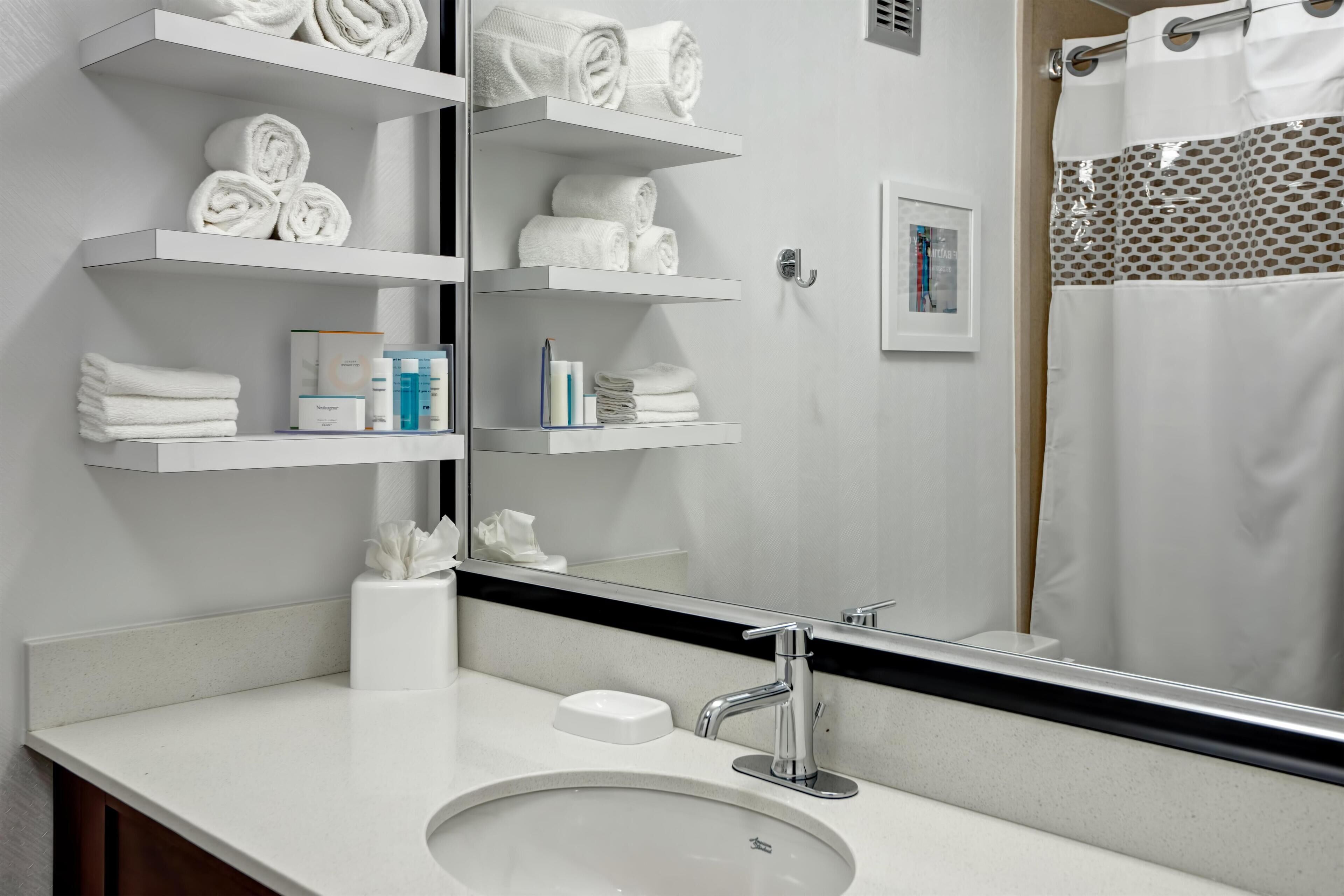 A bathroom with a white sink, a mirror, and shelves holding towels and toiletries.