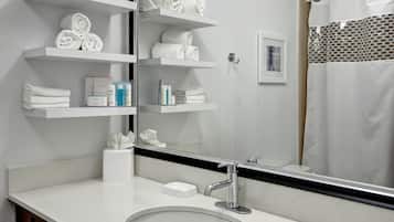 A bathroom with a white sink, a mirror, and shelves holding towels and toiletries.