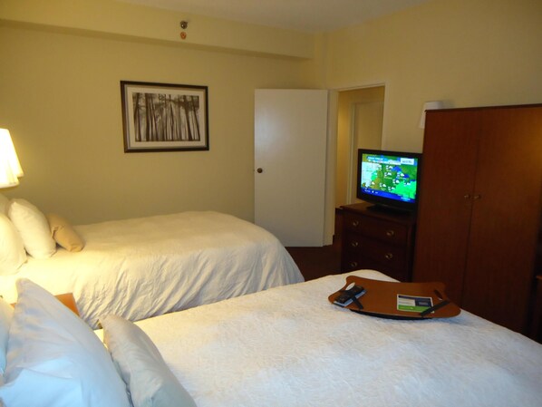 A hotel room with two beds, a television on a dresser, a framed picture on the wall, and a wooden wardrobe.