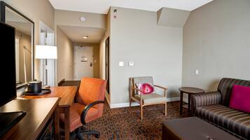 A hotel room with a wooden desk, a television, a sofa, a chair, and a patterned carpet.