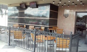An outdoor seating area with tables and chairs, a glass wall reflecting the surroundings, and a sign for 'Jimmy's'. - Imperial Swan Hotel & Suites (Lakeland)