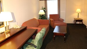 A hotel room with a wooden desk, a green armchair, a red armchair, a small table, and a lamp. - Imperial Swan Hotel & Suites (Lakeland)
