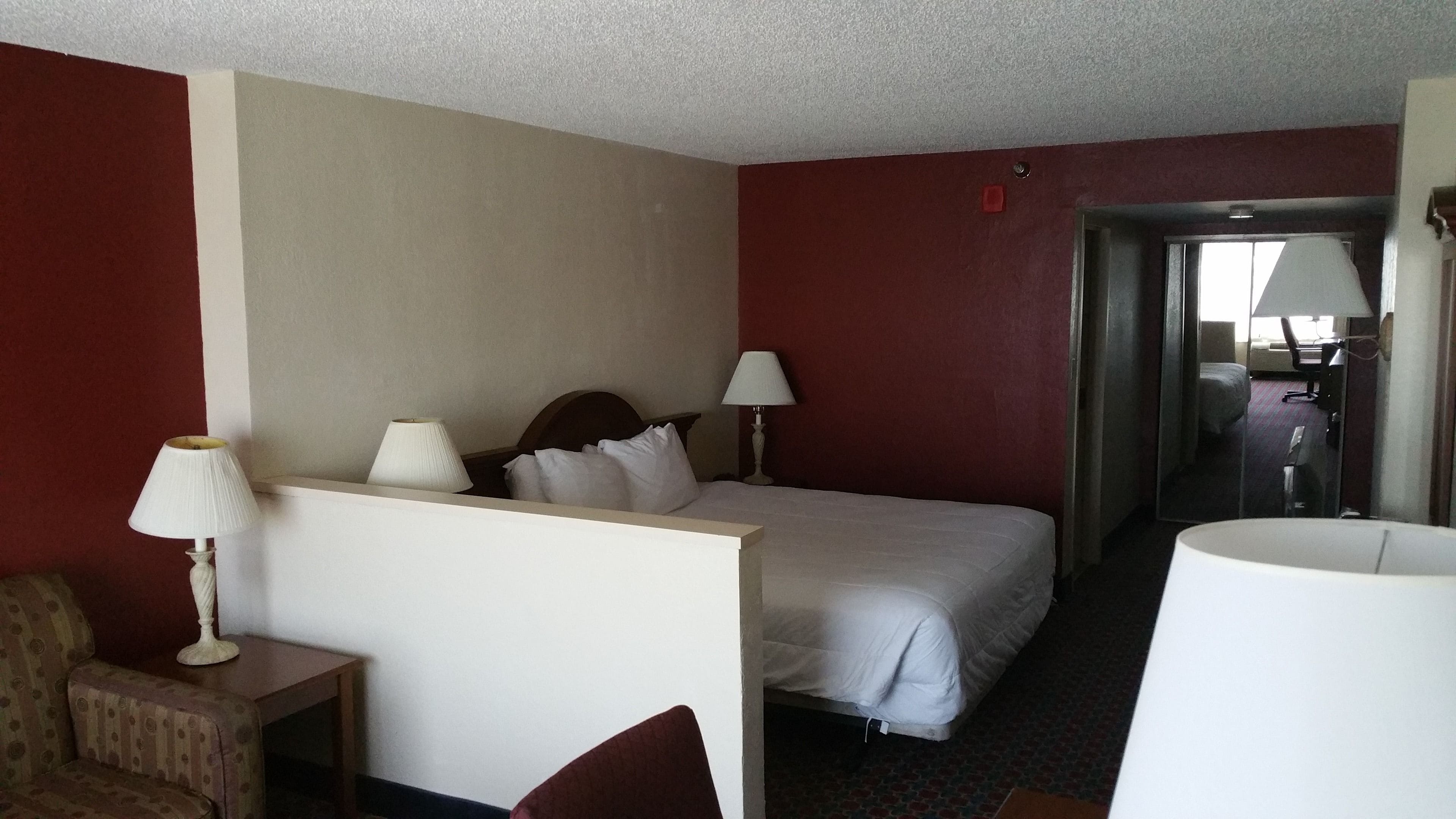 A hotel room with a bed, two bedside lamps, a chair, and a desk.