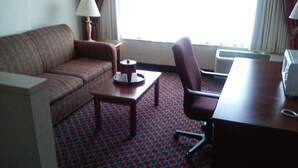 A hotel room with a sofa, a small table, a chair, a lamp, and a desk. - Imperial Swan Hotel & Suites (Lakeland)