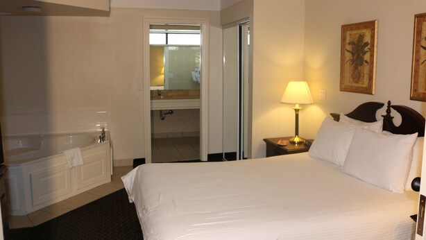 A hotel room with a large bed, a bathroom with a bathtub, and a nightstand with a lamp. - Imperial Swan Hotel & Suites (Lakeland)
