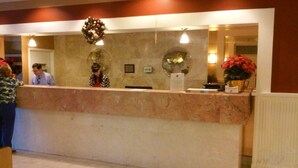 A reception desk with a marble counter, a decorative wreath, and a potted plant. - Imperial Swan Hotel & Suites (Lakeland)