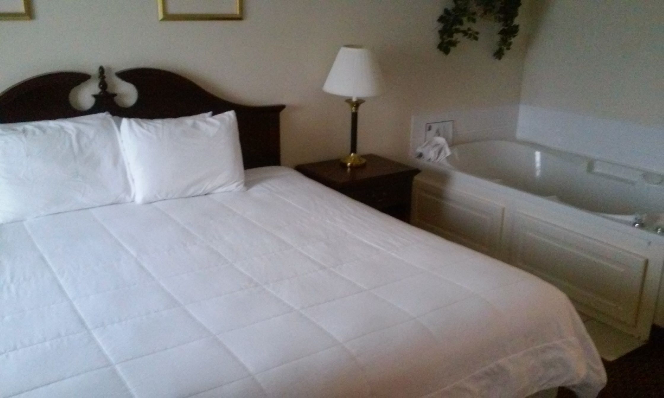A neatly made bed with white linens, a bedside lamp, and a bathroom with a bathtub.