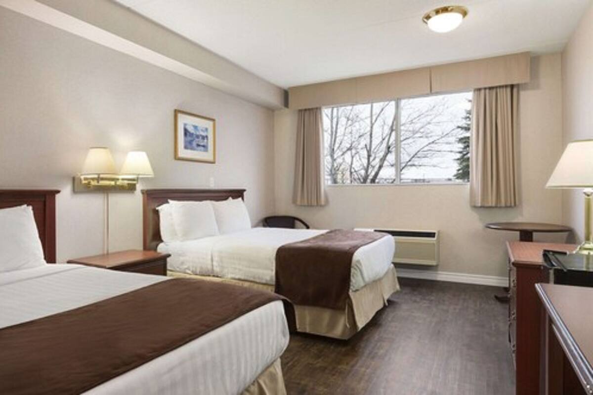 Ein Hotelzimmer mit zwei Betten, einem Schreibtisch, einem Stuhl, einem fenster mit Vorhängen und einem Bild in einem Rahmen an der Wand.