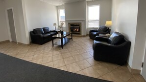 A spacious living room with a fireplace, two black leather sofas, a coffee table, and a lamp. - SureStay by Best Western Brockville (Brockville)