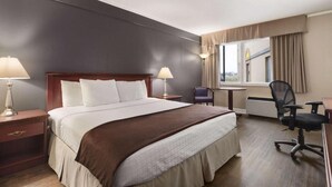 A hotel room with a large bed, two bedside tables with lamps, a desk, a chair, and a window with curtains. - SureStay by Best Western Brockville (Brockville)