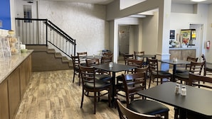 Un espace repas avec des tables et des chaises en bois, un comptoir de cuisine et un escalier menant à un autre niveau.